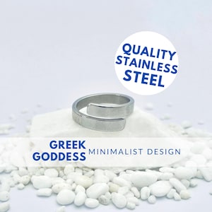 Puede incluir: Un anillo minimalista plateado con un diseño simple. El anillo está hecho de acero inoxidable de calidad y está etiquetado como "Diosa griega" y "Diseño minimalista".