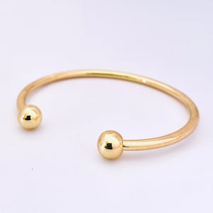May include: A gold bangle bracelet with two round ball ends.