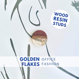 Op de afbeelding: Een ronde houten en hars oorbel met gouden vlokken ingebed in de hars. De oorbel is op een witte achtergrond met zwarte lijnen. De tekst "WOOD RESIN STUDS" staat in een witte cirkel met blauwe tekst. De tekst "GOLDEN FLAKES OFFICE FASHION" staat in een witte rechthoek met blauwe tekst.