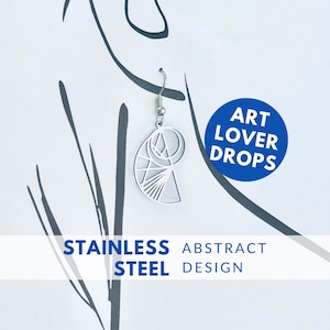 Puede incluir: Un pendiente de acero inoxidable plateado con un diseño geométrico abstracto. El pendiente cuelga de un gancho plateado. La imagen incluye el texto "ART LOVER DROPS" y "STAINLESS STEEL ABSTRACT DESIGN".