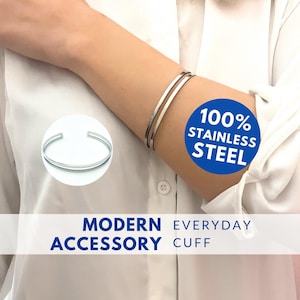 May include: A silver double-band cuff bracelet made of 100% stainless steel. The bracelet is shown on a person's arm. The text "MODERN EVERYDAY ACCESSORY CUFF" is displayed below the image.