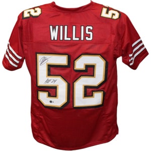 May include: A red football jersey featuring the name WILLIS and the number 52 in white with black and gold trim on the back. The number 52 includes a black ink signature and the inscription HOF 24. The sleeves have three white stripes.