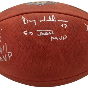 May include: A brown leather football signed by two NFL players. The signatures are in white ink and read "Peyton Manning 17" and "Mark Rypien 11 SB XXVI MVP". The football also has the text "SB XXVIII MVP" written on it.