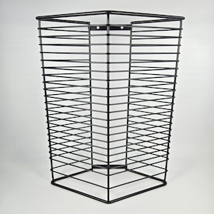 May include: A black metal wire basket with a square top and base, and a rectangular shape. The basket is made of horizontal and vertical wires, creating a grid-like pattern. The basket is empty and sits against a white background.