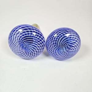 May include: Two round glass cabinet knobs featuring a swirling pattern of deep blue and white lines. The glass has a smooth, polished surface with a spiral design that converges toward the center of each knob, creating a distinct visual effect.