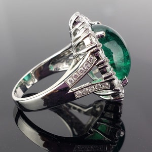 May include: A silver ring with a large green gemstone surrounded by smaller clear gemstones.