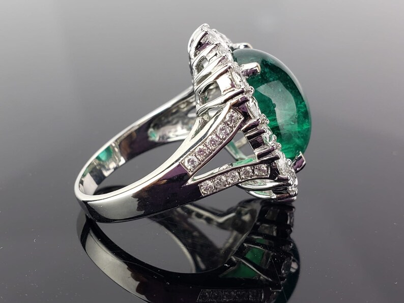 May include: A silver ring with a large green gemstone surrounded by smaller clear gemstones.