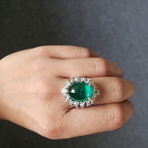 May include: A silver ring with a large, oval-shaped emerald green gemstone surrounded by smaller, clear gemstones.