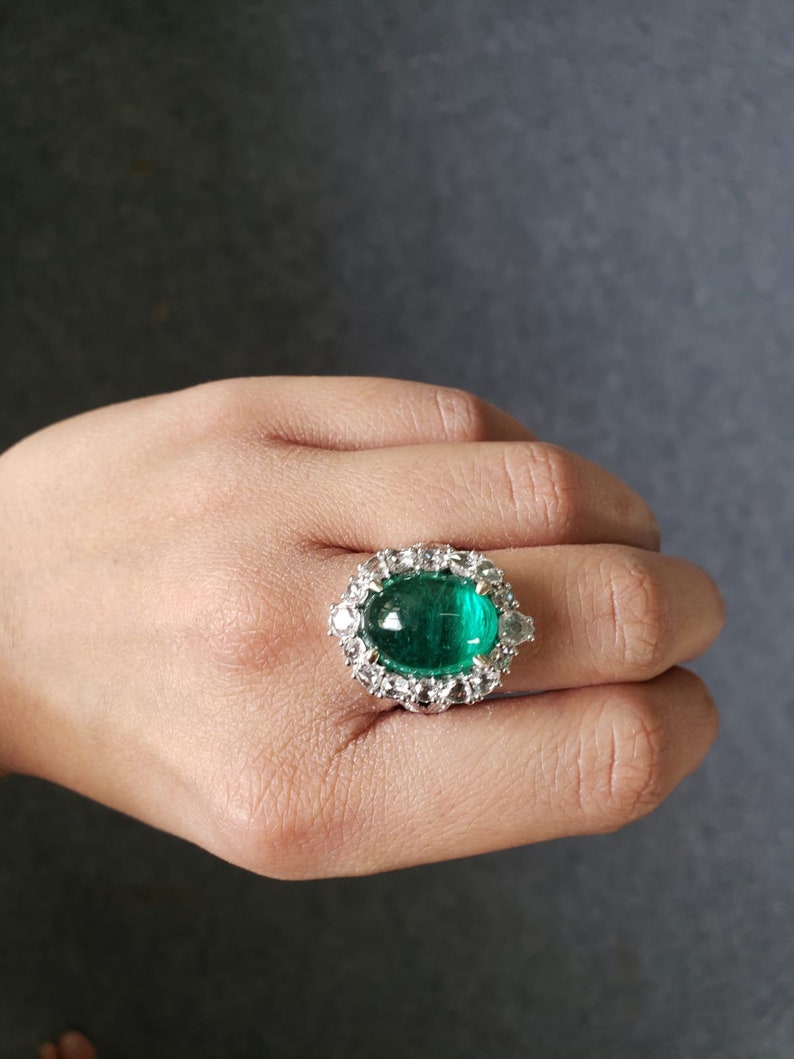 May include: A silver ring with a large, oval-shaped emerald green gemstone surrounded by smaller, clear gemstones.