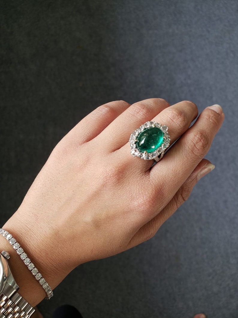 May include: A ring with a large, oval-shaped emerald gemstone surrounded by smaller diamonds. The ring is set in white gold.