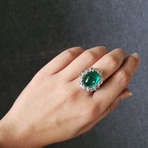 May include: A silver ring with a large, oval-shaped emerald gemstone surrounded by smaller diamonds.