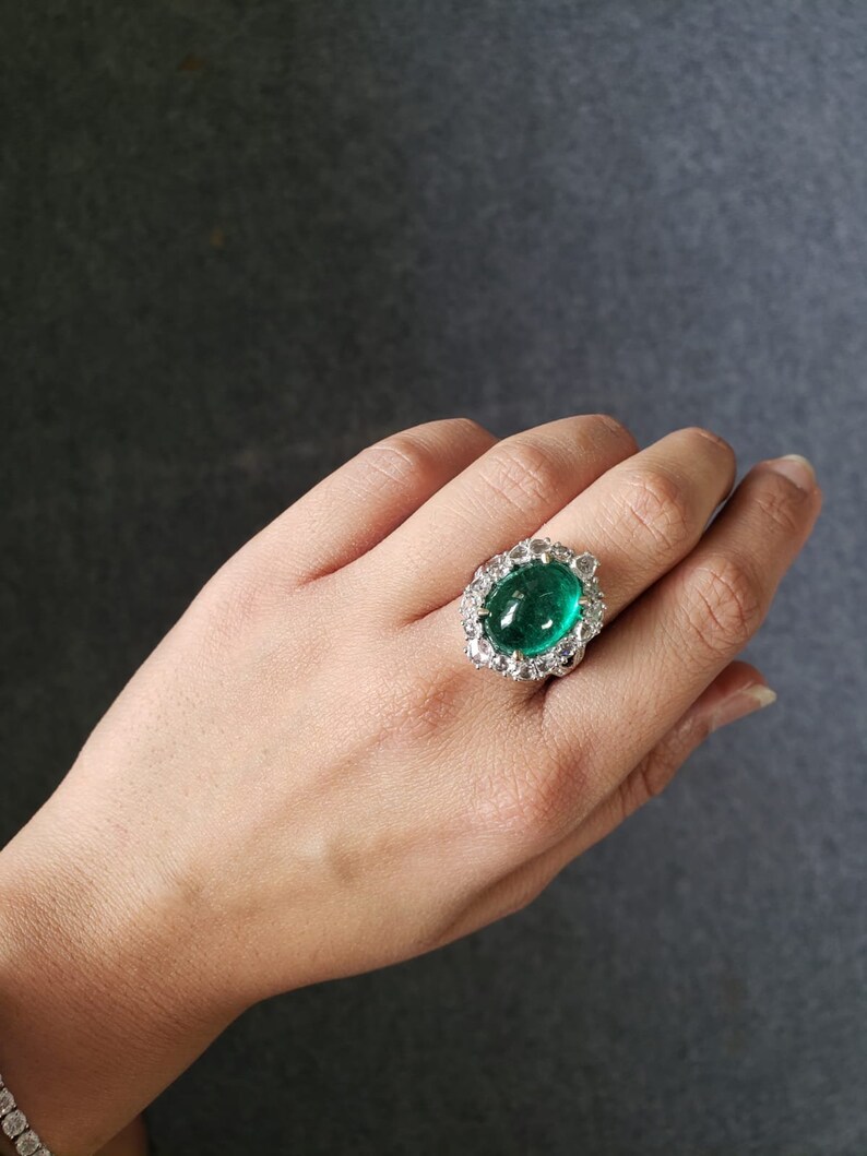 May include: A silver ring with a large, oval-shaped emerald gemstone surrounded by smaller diamonds.