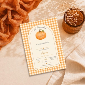Op de afbeelding: Een rechthoekige verjaardagsuitnodiging met een oranje en wit gingham-patroon als achtergrond. In het midden staat een geschulpt boogframe met een illustratie van een pompoen en de tekst A LITTLE PUMPKIN IS TURNING TWO.