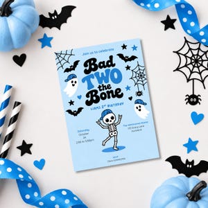 Op de afbeelding: Een lichtblauwe, rechthoekige verjaardagsuitnodigingskaart met de tekst Bad TWO the Bone, Liams 2nd Birthday en evenementdetails. Het ontwerp bevat illustraties van een skelet, spoken, vleermuizen, spinnen en spinnenwebben in zwart en blauw.