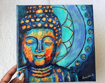 May include: A painting of a blue and orange Buddha with closed eyes. The Buddha is surrounded by a blue and gold mandala. The painting is signed "Aousha '17".