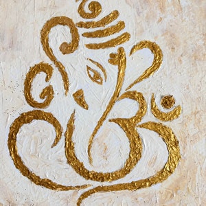 Op de afbeelding: Een gouden Ganesha-schilderij op een gestructureerde witte achtergrond. Het schilderij is een gestileerde afbeelding van de hindoe-god Ganesha, bekend om zijn olifantenkop en slurf.