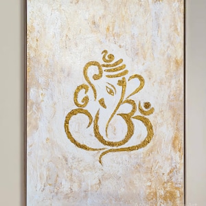 Op de afbeelding: Een gouden Ganesha-schilderij op een wit canvas met een textuur achtergrond. Het schilderij is ingelijst in een lichtbruin frame. De handtekening van de kunstenaar is zichtbaar in de rechter benedenhoek.