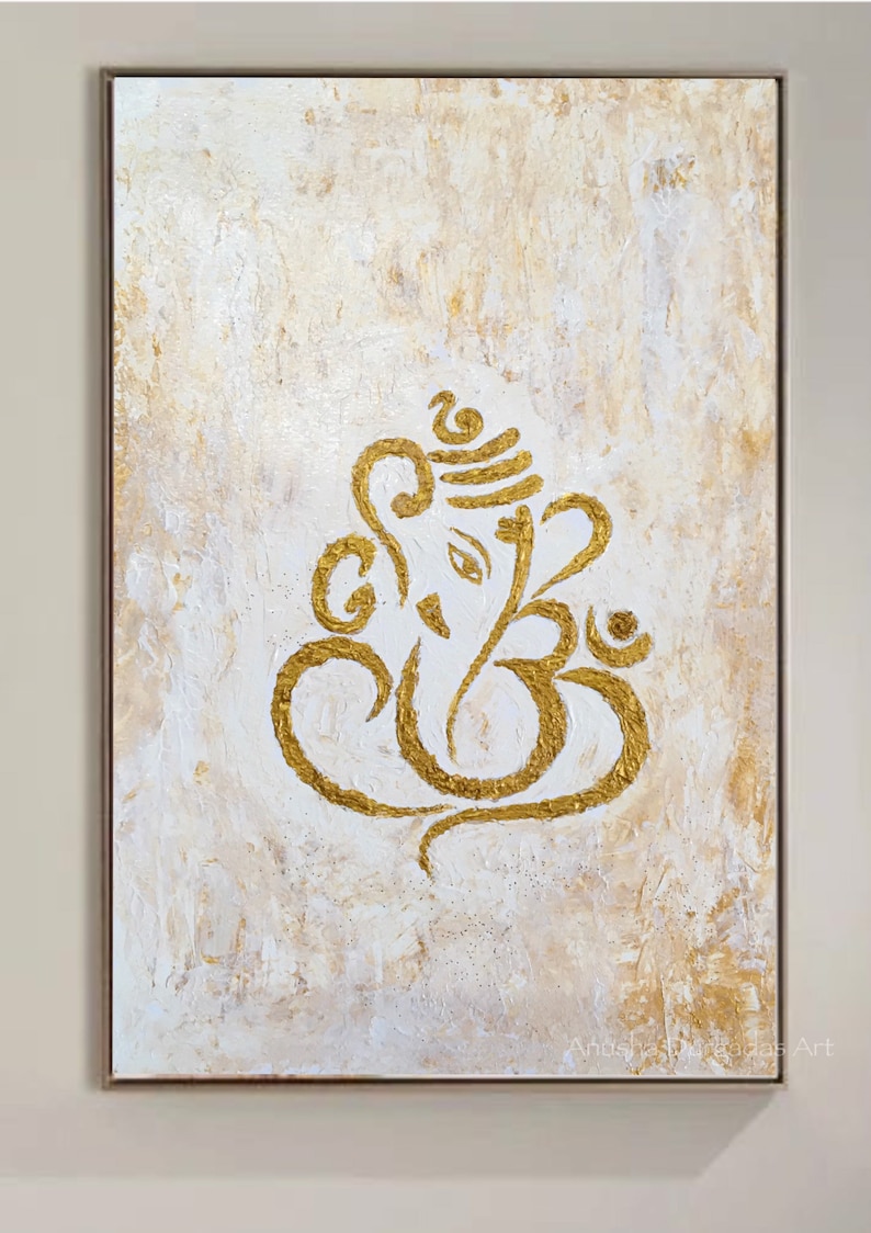 Op de afbeelding: Een gouden Ganesha-schilderij op een wit canvas met een textuur achtergrond. Het schilderij is ingelijst in een lichtbruin frame. De handtekening van de kunstenaar is zichtbaar in de rechter benedenhoek.