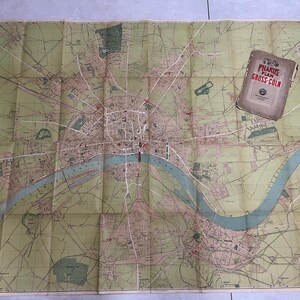 May include: A vintage map of Gross-Cöln, Germany, with a river winding through the city. The map is folded and has a small booklet titled "Pharus-Plan Gross-Cöln" on top.