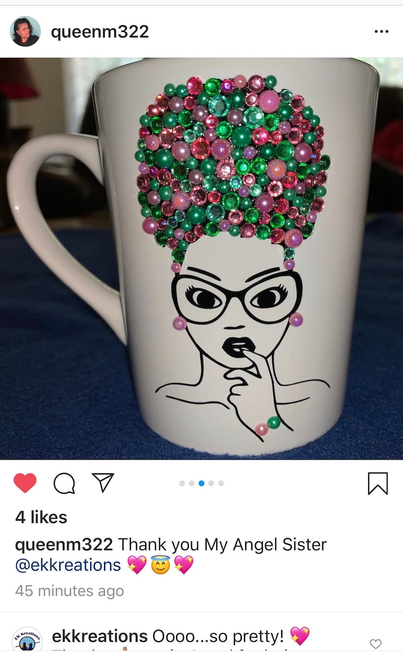May include: White ceramic mug with a black line drawing of a woman with glasses and a pink and green rhinestone afro. The mug is decorated with pink and green rhinestones.