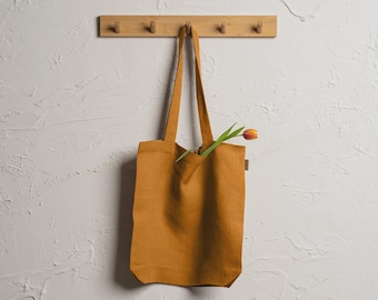 May include: A mustard yellow tote bag hanging on a wooden rack with a single orange tulip sticking out of the top.
