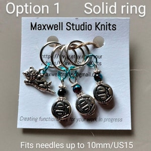 May include: A set of silver knitting stitch markers on a white card. The markers include a cat charm and charms with the number 10. The card reads "Maxwell Studio Knits" and "Fits needles up to 10mm/US15."