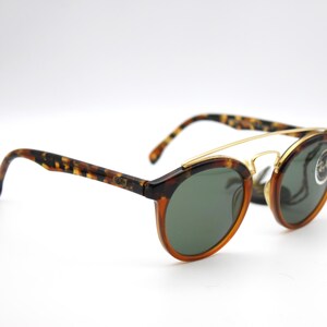 May include: Tortoise shell frame sunglasses with gold accents and green lenses. The sunglasses have a double bridge and a Ray-Ban logo on the right lens.