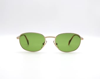 Puede incluir: Gafas de sol con montura dorada y lentes verdes. Las gafas tienen una forma ovalada clásica.