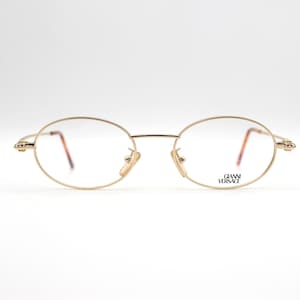 Puede incluir: Gafas ovaladas de metal dorado con un fino marco metálico. El nombre de la marca "GIANNI VERSACE" está impreso en la patilla derecha.