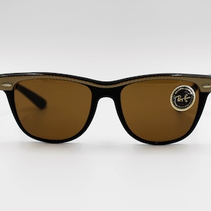 May include: Brown sunglasses with gold accents and a Ray-Ban logo on the right lens.