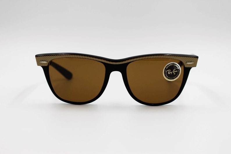 May include: Brown sunglasses with gold accents and a Ray-Ban logo on the right lens.