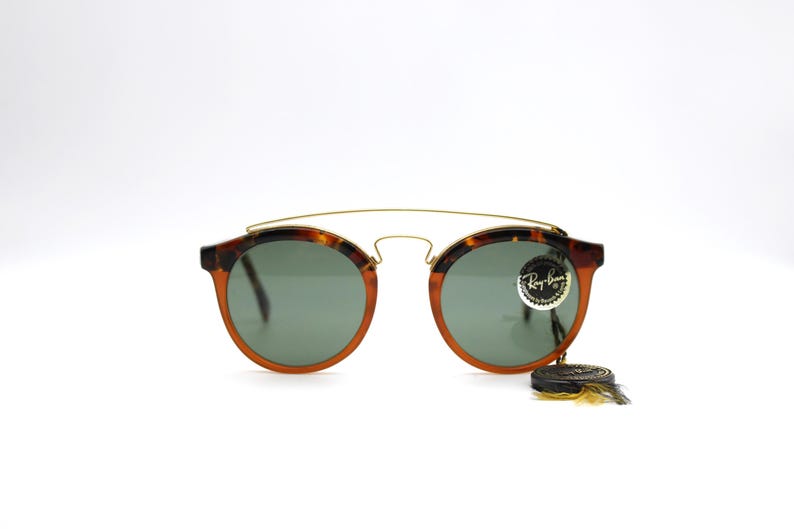 May include: Tortoise shell Ray-Ban sunglasses with green lenses and a gold metal bridge. The sunglasses have a Ray-Ban logo on the right lens.
