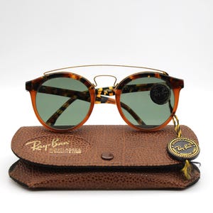 May include: Tortoise shell Ray-Ban sunglasses with green lenses and a gold metal bridge. The sunglasses are in a brown leather case with the Ray-Ban logo.