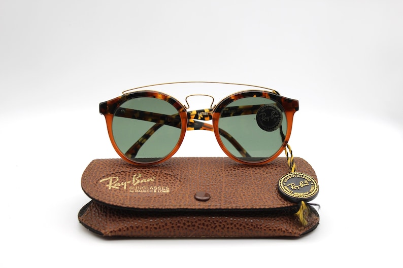 May include: Tortoise shell Ray-Ban sunglasses with green lenses and a gold metal bridge. The sunglasses are in a brown leather case with the Ray-Ban logo.