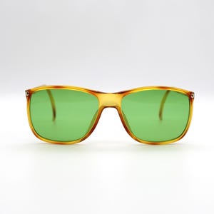 May include: Square-framed sunglasses with a tortoiseshell pattern on the frame and bright green lenses. The glasses have a classic, retro design, suitable for various face shapes. The lenses are a vibrant green color.