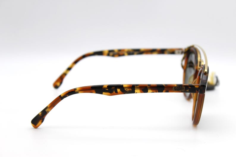 May include: Tortoise shell sunglasses with gold accents and a brown lens. The sunglasses have a thin metal frame and a tortoiseshell pattern on the arms.