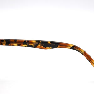 May include: Close-up of the tortoiseshell temple arm of a pair of eyeglasses. The arm is made of plastic and has a brown and black pattern. The text "8267 54 18" is printed on the arm.
