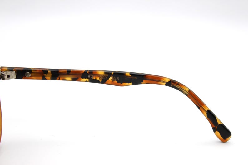 May include: Close-up of the tortoiseshell temple arm of a pair of eyeglasses. The arm is made of plastic and has a brown and black pattern. The text "8267 54 18" is printed on the arm.