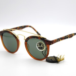 May include: Tortoise shell frame sunglasses with gold accents and green lenses. The sunglasses have a Ray-Ban logo on the right lens.