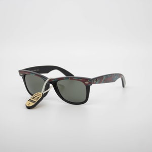 May include: Black sunglasses with a patterned design on the frames. The frames have a mix of red, teal, and black colors. The sunglasses have a tag attached with text. The lenses are dark gray.