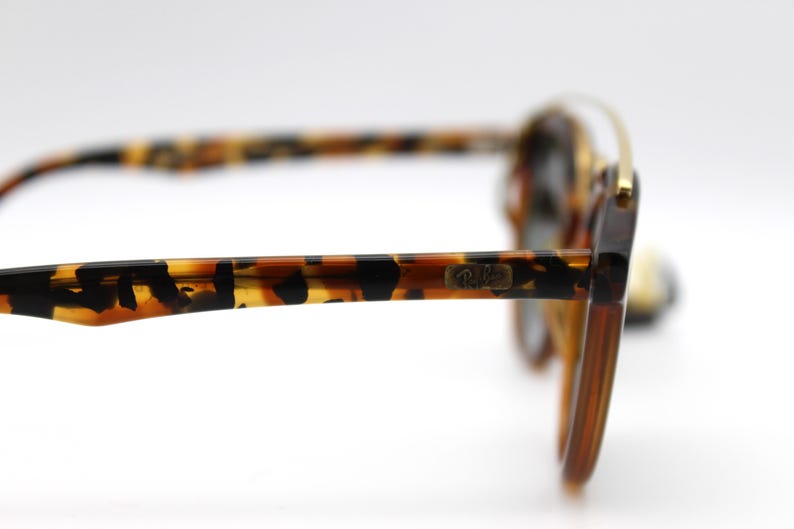 May include: Tortoise shell sunglasses with gold accents and the Ray-Ban logo on the side.