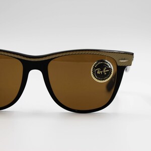 May include: Brown Ray-Ban sunglasses with a gold-colored frame and a gold sticker that says "Ray-Ban" on the right lens.