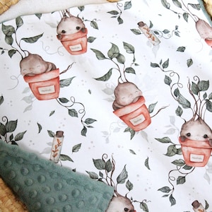 May include: White baby blanket with a whimsical pattern of smiling root creatures in terracotta pots, surrounded by green leaves and vines. The blanket has a soft, textured teal border.