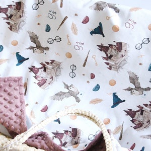 May include: A white baby blanket with a whimsical pattern featuring a castle, owls, glasses, keys, feathers, and wands. The blanket has a soft, pink minky backing.