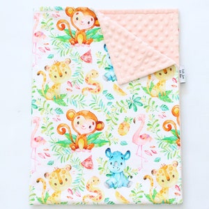 Op de afbeelding: Een wit babydekentje met een jungle dierenprint. Het dekentje heeft apen, luipaarden, een neushoorn, een flamingo en slangen. De achterkant van het dekentje is van zacht, roze minky stof.
