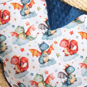May include: A white baby blanket with a blue minky backing features a repeating pattern of red and blue dragons with stars and clouds.