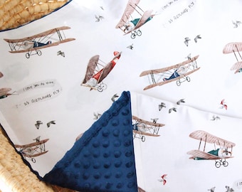 May include: A white baby blanket with a blue minky backing. The blanket features a repeating pattern of vintage airplanes and the text "I love you as high as airplanes fly".