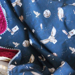 May include: A blue baby blanket with a white owl and moon pattern. The blanket has a pink velvet backing with a gray trim.