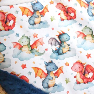 May include: A white fabric with a repeating pattern of blue, green, and red dragons on clouds with orange and white stars. The fabric has a blue border.