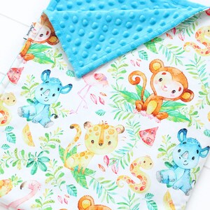 Op de afbeelding: Een witte babydeken met een blauwe minky-rug. De deken heeft een kleurrijke jungledierenprint met apen, neushoorns, slangen en flamingo's.